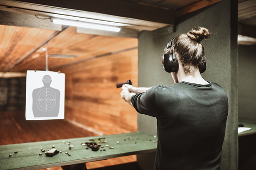 Hombre moderno con moño de pelo tomando un tiro con arma en el blanco a distancia de la pistola photo