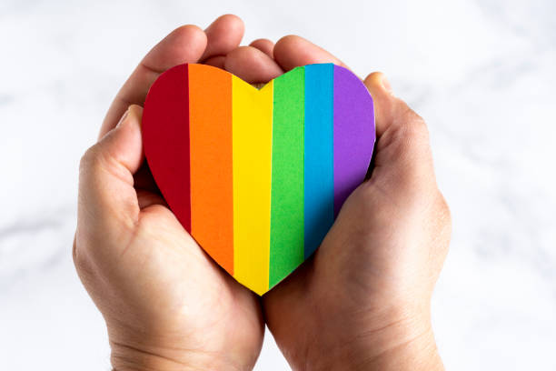 Close up of a person's hands holding a heart with the colored stripes representing the LGBT community. stock photo