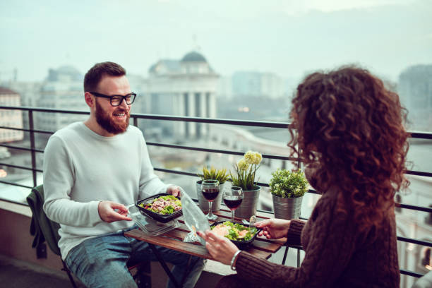 Couple Enjoying Salad Dinner During Rooftop Date Couple Enjoying Salad Dinner During Rooftop Date caesar salad food salad tuna stock pictures, royalty-free photos & images