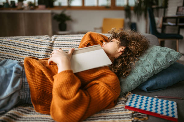 Afternoon napping Young pretty student woman napping on the sofa in her living room after studying napping stock pictures, royalty-free photos & images