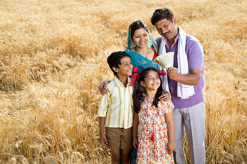Happy family with farmer holding Indian rupee notes on agricultural field