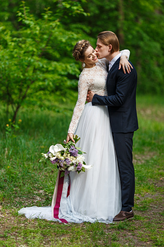 Groom and bride holding wedding bouquet with lilac flowers. Happy couple on spring wedding walk.