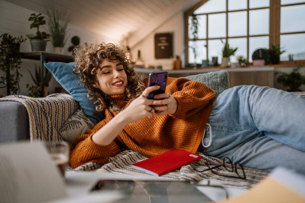 donna che usa lo smartphone per i social media sdraiati sul suo divano - silence curly hair facial expression female foto e immagini stock