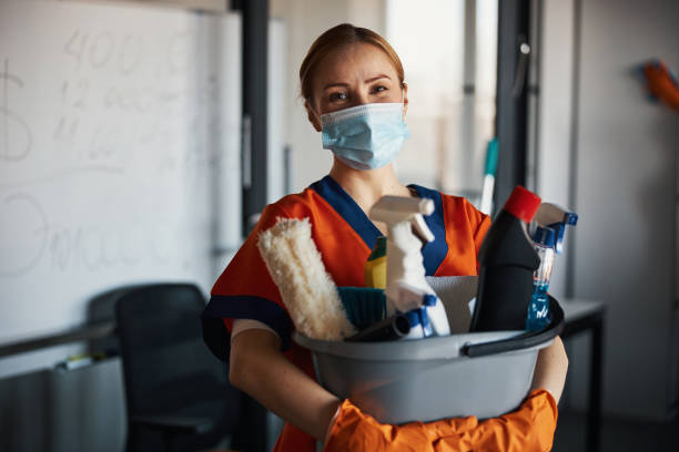 Cleaner in a face mask showing her cleaning products Cropped photo of a woman holding a plastic bucket with janitorial supplies with both hands cleaner stock pictures, royalty-free photos & images