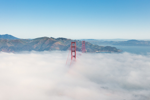 Aerial View of Golden Gate Bridge rising up through the fog. Fog billowing over the Bridge on a blue sky day.