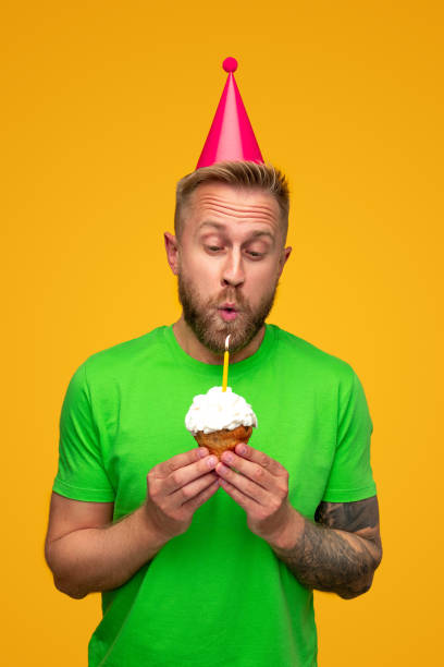 istock Happy man blowing out candle on cupcake 1313331006