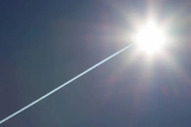 Airplane flies leaving contrail trace with a bright sun in the sky