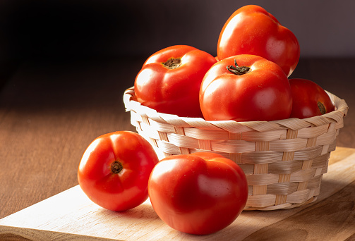 Tomatoes, beautiful tomatoes arranged in a basket and on wood, dark background, selective focus.