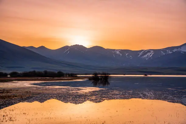 Photo of Beautiful bright sunrise over the lake and mountains, reflection in the water. Panoramic view.