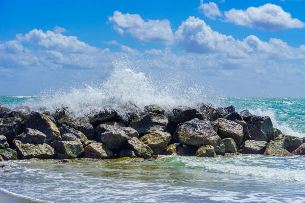 An ocean wave crashes and breaks over a rock breakwater