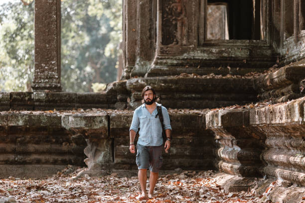 hombre parado junto a una ruina en ankor wat park - ankor fotografías e imágenes de stock