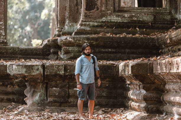 hombre parado junto a una ruina en ankor wat park - ankor fotografías e imágenes de stock