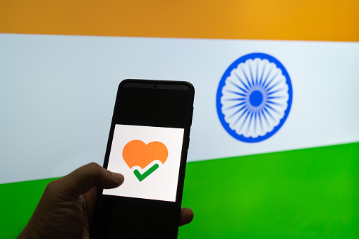 Man holding mobile phone with the arogya setu app in front of a flag of India showing how technology is helping contact tracing in covid 19 pandemic
