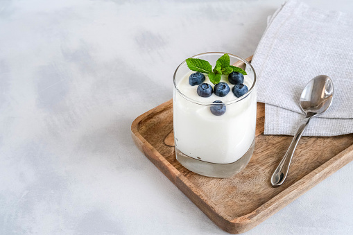 Homemade Greek yogurt in a glass. White yogurt in glass with fresh blueberry on a wooden tray