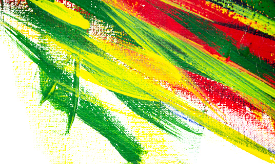 Background from different strokes of red, yellow, green and blue paint with brush on white background close-up. Bright colorful backdrop of brush lines. Mixing color streaks of paint on white canvas