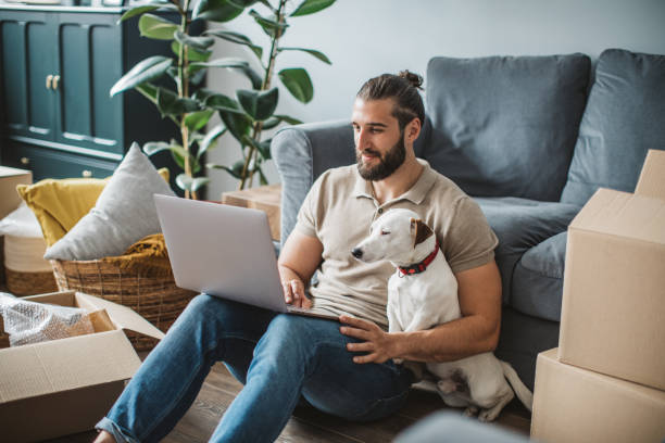 Moving day Young men moving in new house. He is happy and using laptop to organize everything. His pet dog is with him. man 30 years old stock pictures, royalty-free photos & images