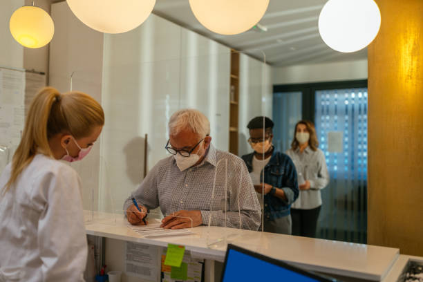 People filling in documentation in the hospital Photo of senior man filling in a document about the appointment in the doctor's office. medical office lobby stock pictures, royalty-free photos & images