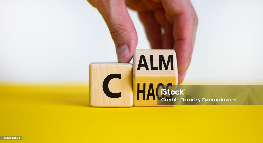 Stop chaos, time to calm. Male hand turns a wooden cube and changes the word 'chaos' to 'calm'. Beautiful yellow table, white background, copy space. Business and chaos or calm concept. Chaos Stock Photo