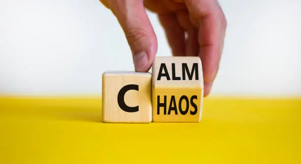 Photo of Stop chaos, time to calm. Male hand turns a wooden cube and changes the word 'chaos' to 'calm'. Beautiful yellow table, white background, copy space. Business and chaos or calm concept.