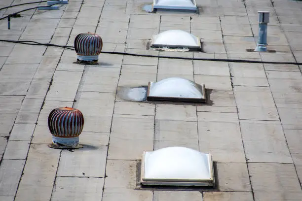 Photo of Ponding water pooling on the settled flat roof, turbine vents and skylight roof windows on the rooftop of an industrial building.