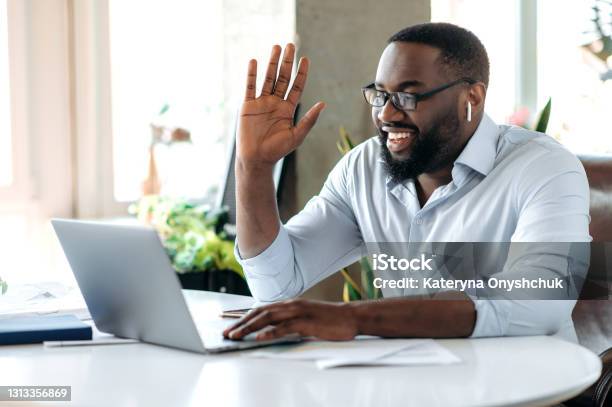 Friendly Confident Successful Young African American Businessman Manager Or Lawyer Working At Laptop Communicate With Employee Or Customer By Video Conference Greeting With Hand Gesture Smile Stock Photo - Download Image Now