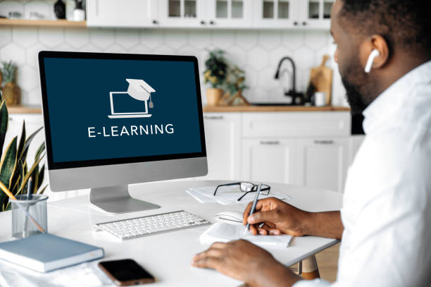 istock Online education, e-learning. African American smart confident guy sitting at home at work desk, uses computer, listening to an online lecture, taking notes, a teacher and diverse people on the screen 1313356893