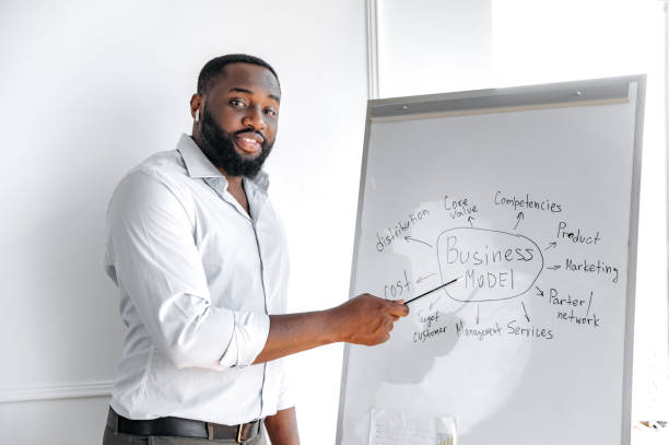 istock Teaching and learning concept. Smart successful african american bearded stylish business coach stands near a whiteboard, looks at the camera, smiles friendly 1313356908