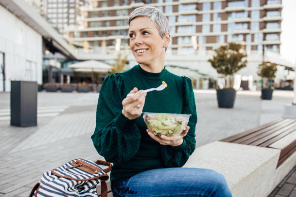 Portrait of a happy woman on a lunch break Portrait of a beautiful woman eating a salad from the plastic box outdoors. lunch break stock pictures, royalty-free photos & images