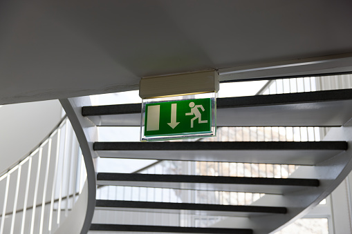 green emergency exit sign under a spiral staircase with railing, by day, without people