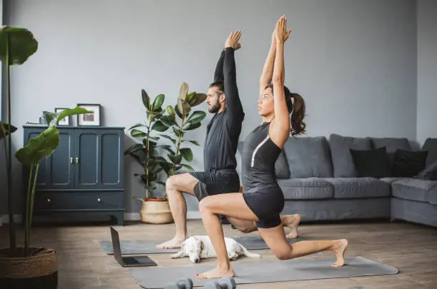 Young couple at home practicing yoga. They are watching online fitness live streaming classes.