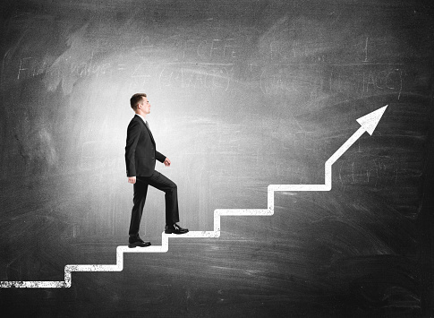 Woman manager in business suit climb up the stairs, background of blackboard with formula. Concept of personal development, personal and career growth and success
