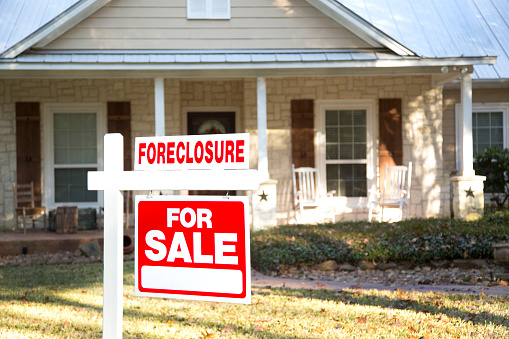 Home for sale with red and white real estate sign during the fall season.  Fall season with leaves on ground.  Front porch and windows in background.  Residential neighborhood.  Moving house, relocation concept.  Foreclosure.