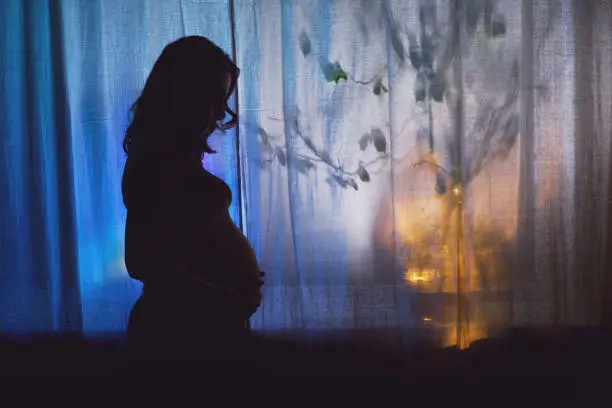 Photo of A woman suffering from insomnia on the background of a night window, silhouette