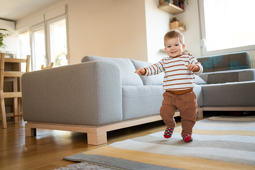 Adorable cheerful Caucasian baby boy walking around the house and looking at camera.