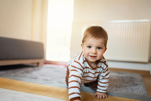 Adorable cheerful Caucasian baby boy crawling at home and looking at camera.