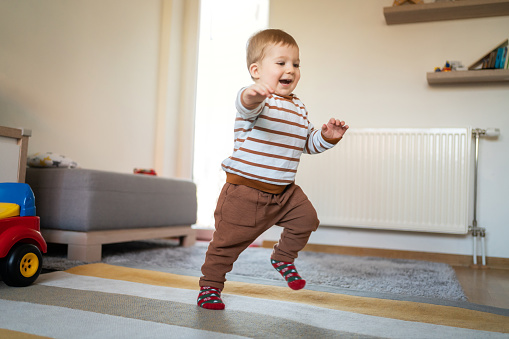 Adorable cheerful Caucasian baby boy walking around the house.