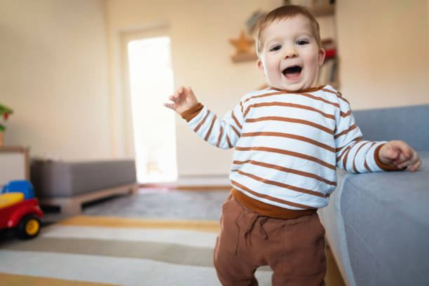 istock Happy Caucasian baby boy making his first steps while holding on the sofa 1313379420