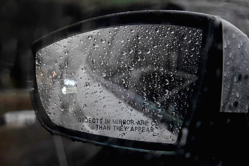Close-up shot of a wet foggy side-view mirror under the rain. There are raindrops all over it, making the reflection unclear.