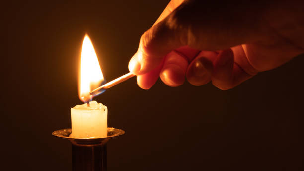 istock Close-up of a hand using a match to light a small half candle, black background 1313388210