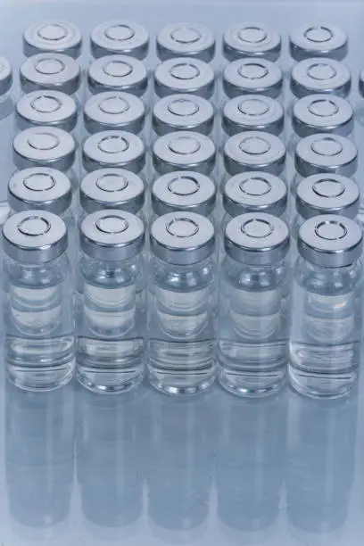 Glass medical ampoule vial for injection. Medicine is dry white drug penicillin powder or liquid with of aqueous solution in ampulla. Close up. Bottles ampule with aluminum cap on backgrounds gray.