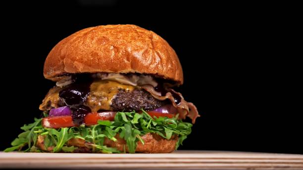 istock Craft burger is cooking on black background. Consist: sauce, arugula, tomato, onion, bacon, currant sauce, ricotta cheese, air bun and marble meat. 1313396867