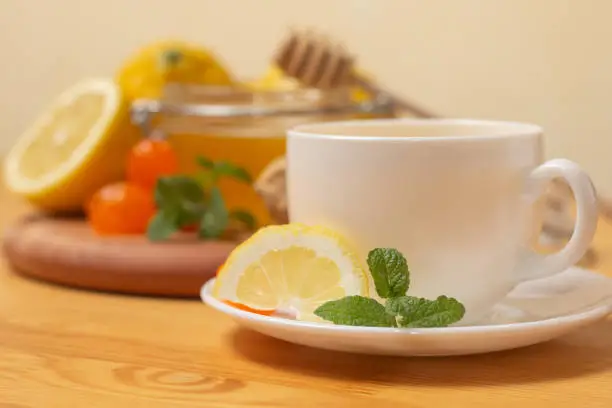 Ginger tea with mint and lemon. Healthy and hot drink. Liquid honey in honey-jar. White cup on wooden background. Selective focus. High quality photo