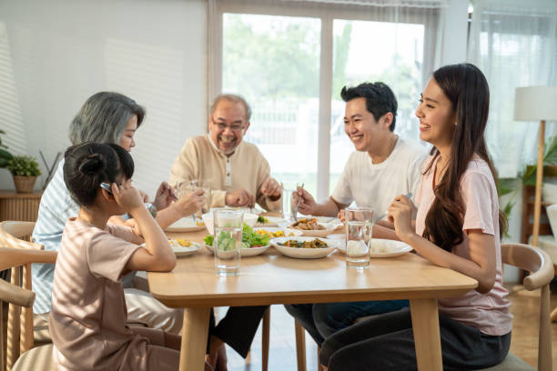 grande família asiática feliz gasta tempo almoçando na mesa de jantar juntos. filha zinha gosta de comer com pai, mãe e avós. relacionamento e atividade de várias gerações em casa - family togetherness eating meal - fotografias e filmes do acervo