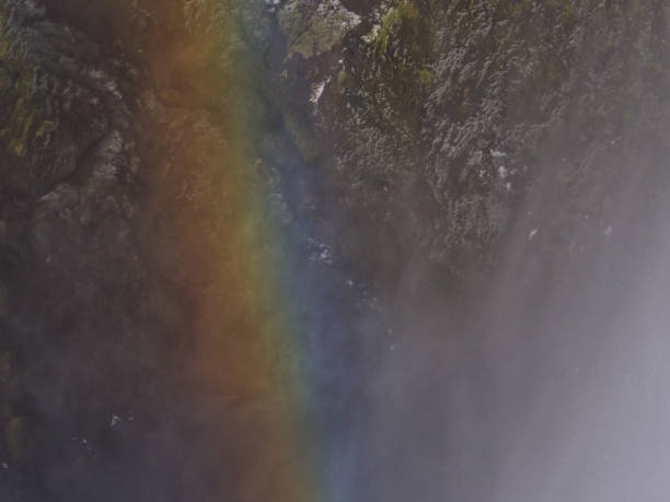 vista ravvicinata dell'arcobaleno colorato nello spruzzo della famosa cascata di skógafoss con faccia di roccia ghiacciata sullo sfondo nella stagione invernale nel sud dell'islanda. - flowing nature spray rock foto e immagini stock