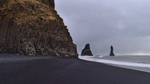 View of famous beach Reynisfjara on the southern coast of Iceland with black pebble stones and basalt rock formations on cloudy winter day with Reynisdrangar rocks. stock photo