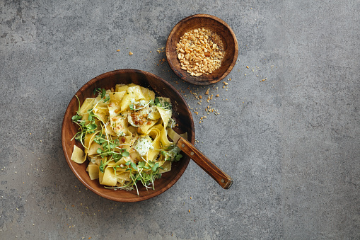Vegetarian Pappardelle with zucchini, eggplant, microgreen and nuts. Flat lay top-down composition on concrete background.
