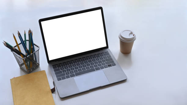 istock Mock up computer laptop with blank screen, notebook, coffee cup and pencil holder on white office desk. 1313404746