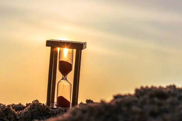 Photo of Time concept Hourglass on sandy beach in summer with sea background