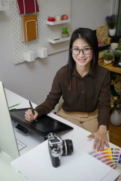 幸せな若い女性グラフィックデザイナーの肖像画は、彼女の職場に座って、カメラに微笑んでいます。 - business person technology digital tablet using computer ストックフォトと画像