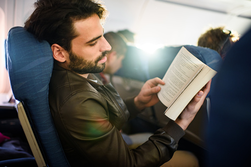 Young man reading a novel while relaxing during his travel in the airplane.